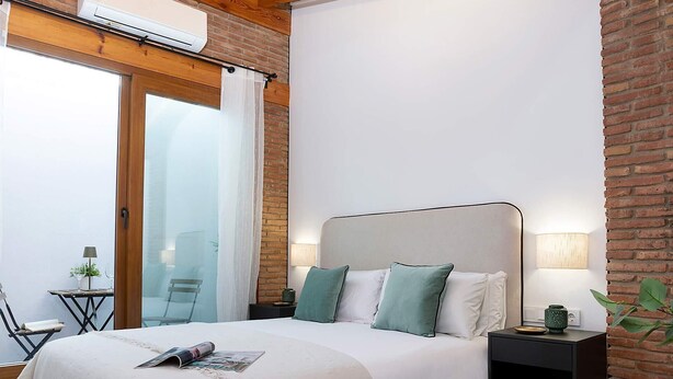 Un dormitorio con una cama grande, una mesita de noche, una lámpara y vistas a través de una puerta de cristal.