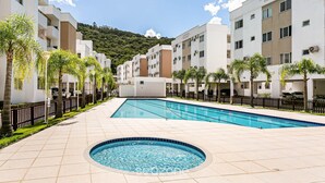 A swimming pool area with a circular hot tub, surrounded by modern buildings and palm trees.