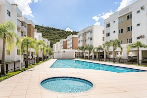 Un área de piscina con un jacuzzi circular, rodeado de edificios modernos y palmeras.