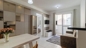 A modern living room with a dining area, a kitchen, and a balcony with a TV.