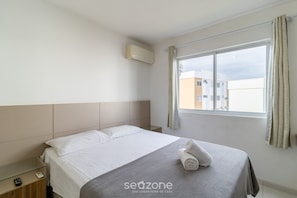 Habitación de hotel con cama, mesita de noche, aire acondicionado y ventana con cortinas.