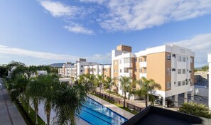 A modern hotel with multiple floors, a swimming pool, and palm trees.