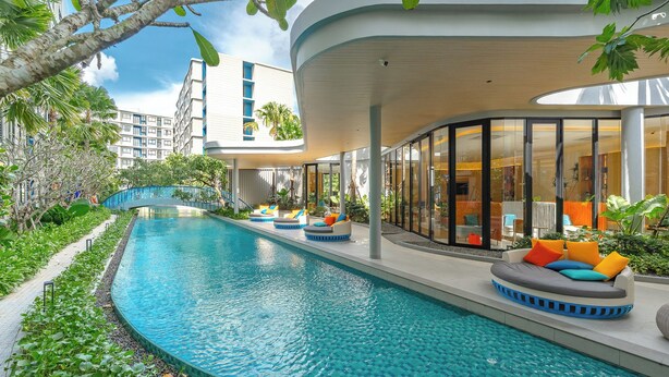 Un hôtel moderne doté d’une piscine, d’un espace extérieur aménagé et d’une zone couverte aux murs de verre.