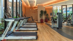 Une salle de sport moderne équipée de tapis de course, d’appareils d’exercice et de grandes fenêtres donnant sur l’extérieur.
