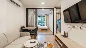 Une chambre d’hôtel compacte comprenant un canapé, une petite table, un téléviseur fixé au mur et une vue sur l’extérieur grâce à une porte coulissante.