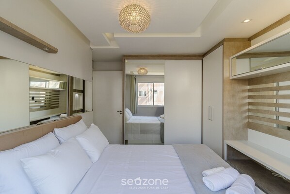 Ein modernes Hotelzimmer mit einem großen Bett, einem begehbaren Kleiderschrank und Blick durch eine Tür.
