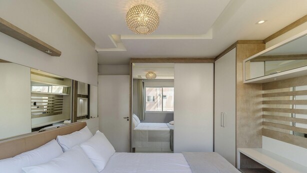 A hotel room with a bed, a large mirror, a wardrobe, and a chandelier. - Apt. w/ Barbecue & Pool in Canasvieiras Rpc0305 (Florianópolis)