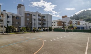 An outdoor basketball court with a net, surrounded by a fence, and adjacent to residential buildings. - Apt. w/ Barbecue & Pool in Canasvieiras Rpc0305 (Florianópolis)