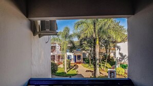 Vista desde un balcón con barandilla, sobre un patio con palmeras y un edificio con puerta azul.