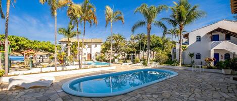 A swimming pool surrounded by stone tiles, palm trees, and a white building with blue accents.