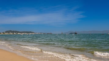 A beach with calm waters, boats, and distant hills.