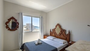 Un dormitorio con cama, cabecera de madera, ventana con vistas a edificios y agua, y un espejo en la pared.