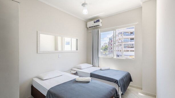 Habitación de hotel con dos camas, un espejo grande, ventilador de techo, unidad de aire acondicionado y ventana con vista a edificios.