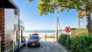 A red car parked in a paved driveway leading to a building with a view of the beach. - 2BR apt W/suite 100m Bombas Beach Ror0001 (Bombinhas)