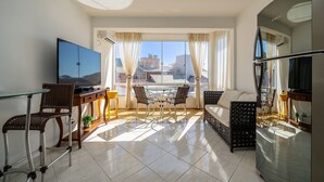 A modern living room with a glass table, wicker chairs, a sofa, a TV, and a view of buildings through large windows. - 2BR apt W/suite 100m Bombas Beach Ror0001 (Bombinhas)