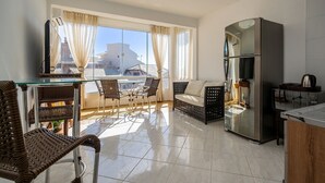 A spacious living area with a glass dining table, wicker furniture, a sofa, and a large window with curtains. - 2BR apt W/suite 100m Bombas Beach Ror0001 (Bombinhas)