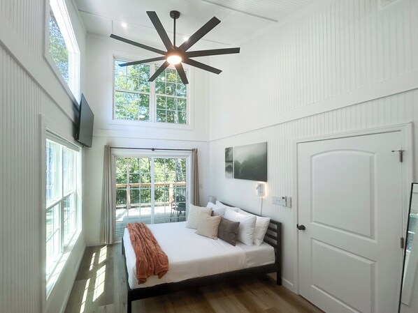 A bedroom with a bed, a ceiling fan, a TV mounted on the wall, and large windows. - Acorn Drop • 2 Full Baths • Hot Tub • <10 Min RRG (Campton)