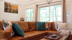 A brown leather sectional sofa with teal and white cushions, a wooden tray with a book, and a white blanket on a matching ottoman. - Acorn Drop • 2 Full Baths • Hot Tub • <10 Min RRG (Campton)