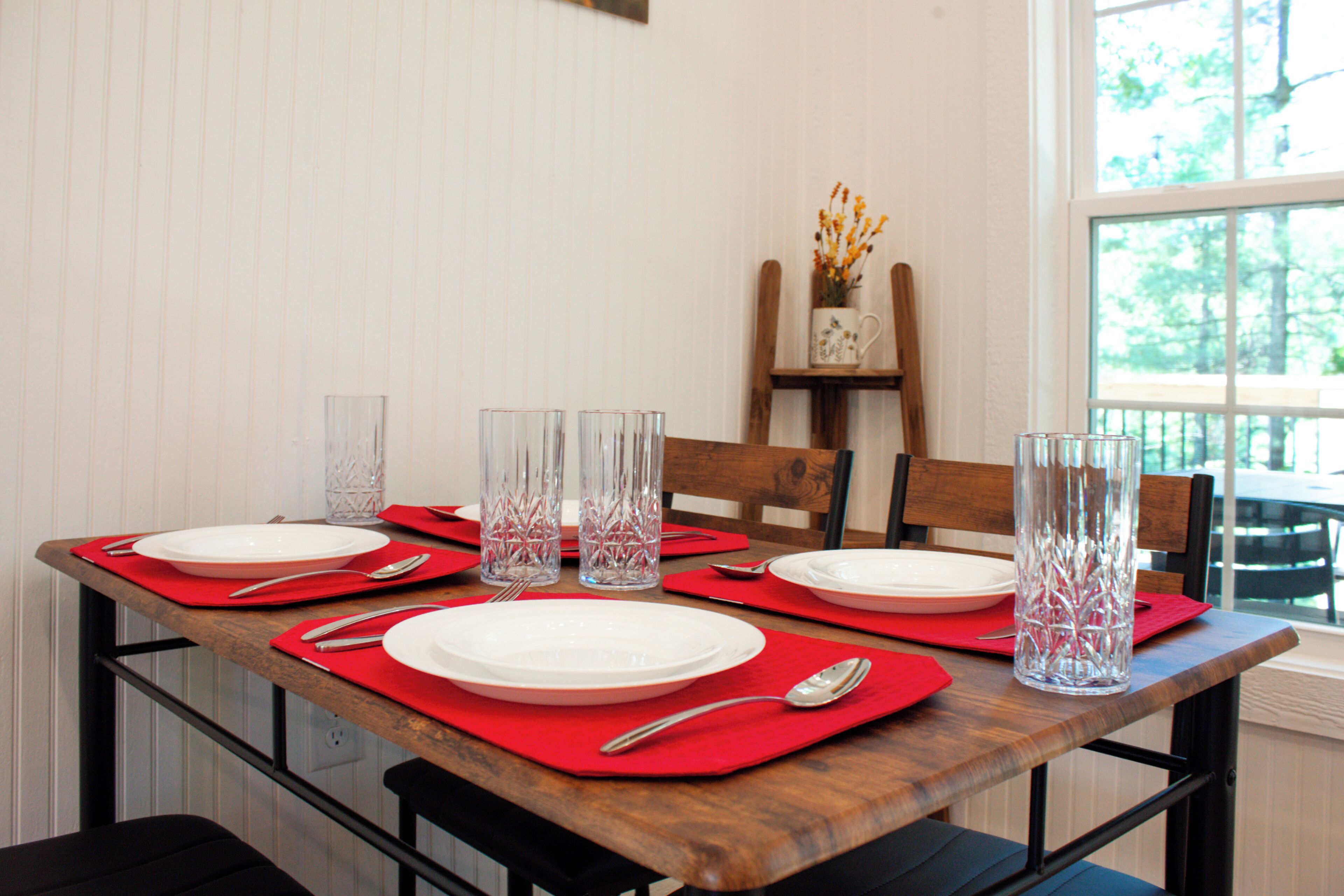 Mesa de comedor dispuesta con individuales rojos, platos blancos y jarras de vidrio transparentes para agua.