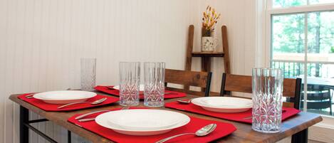 Mesa de comedor dispuesta con individuales rojos, platos blancos y jarras de vidrio transparentes para agua.