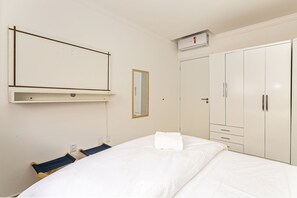 A hotel room with a bed, a wardrobe, a mirror, and a wall-mounted heater. - Modern ap W/pool one Block From the Beach Rmi201 (Florianópolis)