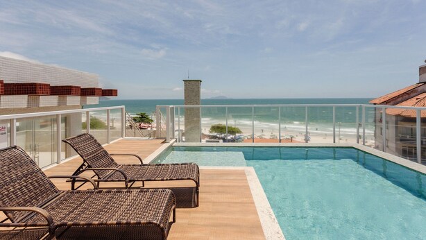A rooftop pool with lounge chairs, a glass balustrade, and a view of the beach. - Modern ap W/pool one Block From the Beach Rmi201 (Florianópolis)