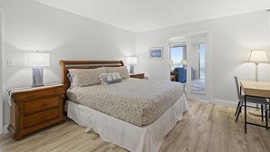 A bedroom with a wooden bed, bedside tables, a desk, and a view of the outside. - 🌊🌑Oceanfront with Incredible Views | Great Amenities | Moontide B103🌑🌊 (New Smyrna Beach)