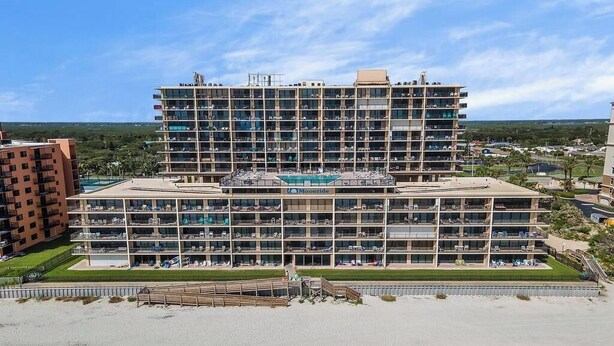 A multi-story hotel with a pool on the ground floor, surrounded by a sandy beach and greenery. - 🌊🌑Oceanfront with Incredible Views | Great Amenities | Moontide B103🌑🌊 (New Smyrna Beach)