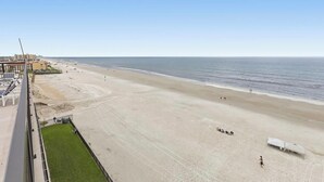 A beach view from a balcony with a clear sky, sandy beach, and a few people. - 🌊🌑Oceanfront with Incredible Views | Great Amenities | Moontide B103🌑🌊 (New Smyrna Beach)