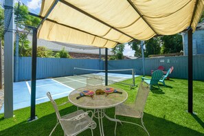 Une terrasse extérieure avec une table et des chaises, un court de tennis et un espace salon abrité.