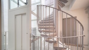 Una escalera de caracol con barandillas metálicas, una puerta en la parte inferior y vistas del piso superior a través de puertas de vidrio.