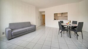 Una sala de estar moderna con un sofá gris, una mesa de comedor con sillas, y una cocina al fondo.