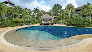 A large, curved swimming pool with a gazebo in the center, surrounded by lush greenery and palm trees. - C215 Bang Tao Beach Garden F21 (Choeng Thale)