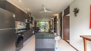 A modern kitchen with a washing machine, a microwave, and a dining area with a view of greenery. - C215 Bang Tao Beach Garden F21 (Choeng Thale)