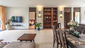 A modern living room with a flat-screen TV, a dining area with a table and chairs, a bookshelf, and a ceiling fan. - C215 Bang Tao Beach Garden F21 (Choeng Thale)