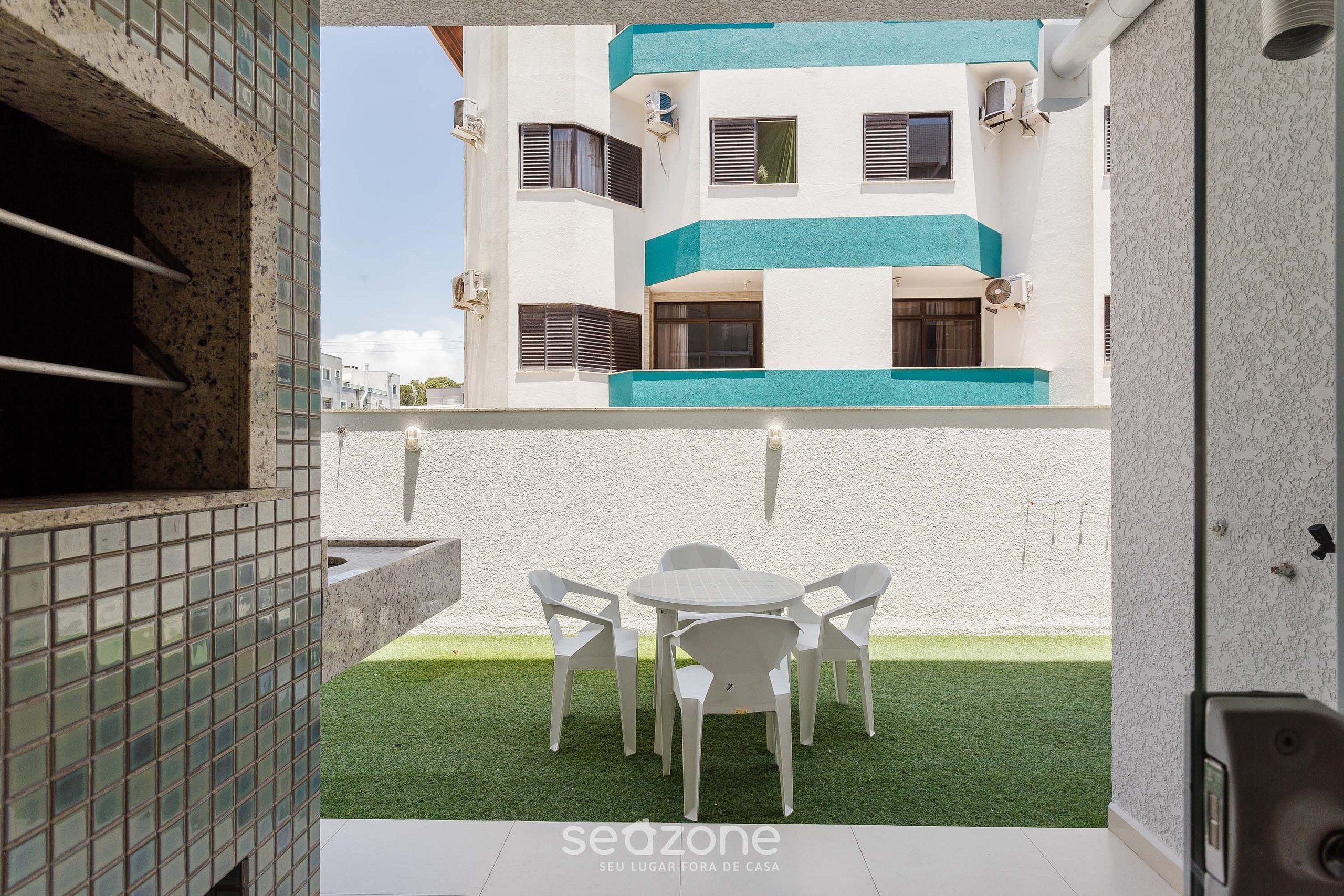 A patio with a table and chairs, a small lawn, and a building with multiple windows and air conditioning units.