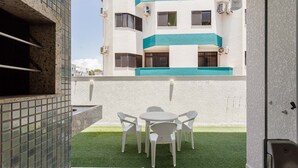 Une terrasse avec une table et des chaises blanches, une petite pelouse et, au fond, un bâtiment doté de balcons.