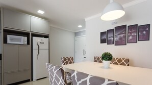 Une cuisine moderne dotée d’appareils électroménagers intégrés, un coin repas avec des chaises à motifs et un luminaire fixé au mur.
