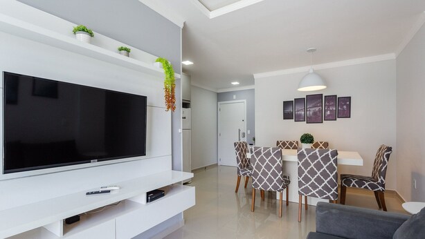 Un salon moderne avec un téléviseur à écran plat, un canapé, un coin repas avec des chaises à motifs et une cuisine en arrière-plan.