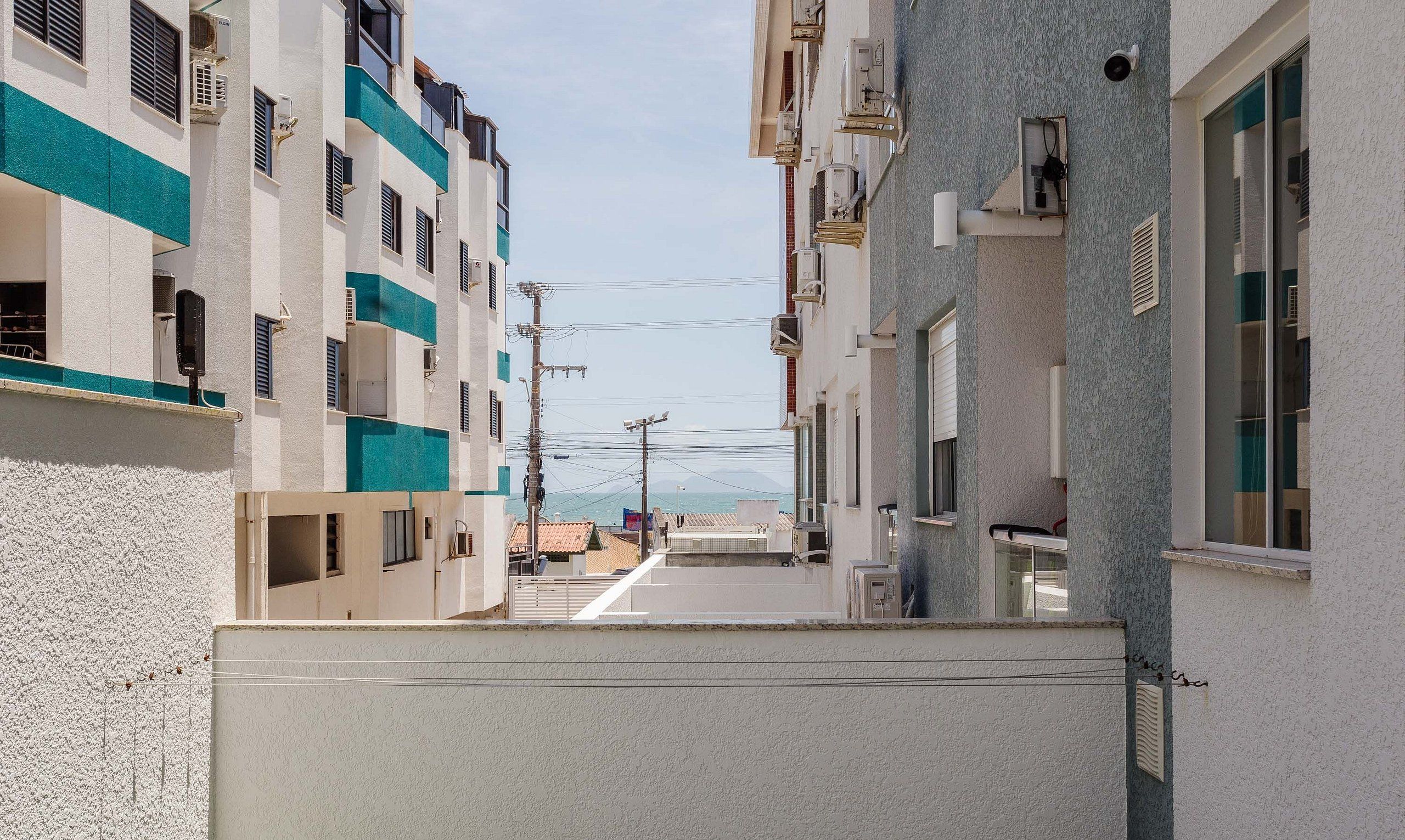 A narrow street between two buildings with balconies, a clear sky, and power lines.