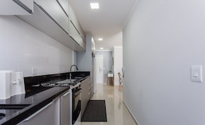 A modern kitchen with white cabinets, a black countertop, and stainless steel appliances. - Beautiful Seaside Apartment With Barbecue Rmi0007 (Florianópolis)