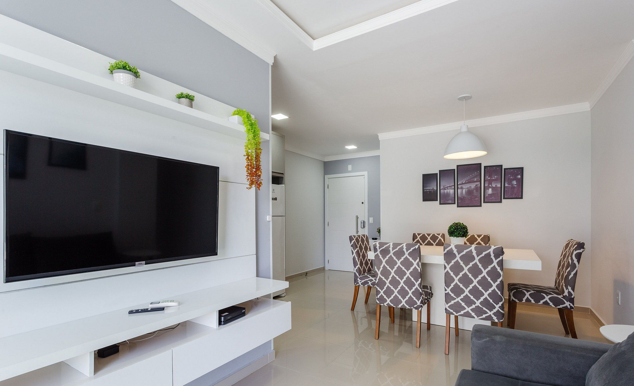 Una sala de estar moderna con un televisor de pantalla plana, un sofá, un comedor con sillas estampadas y una cocina al fondo.