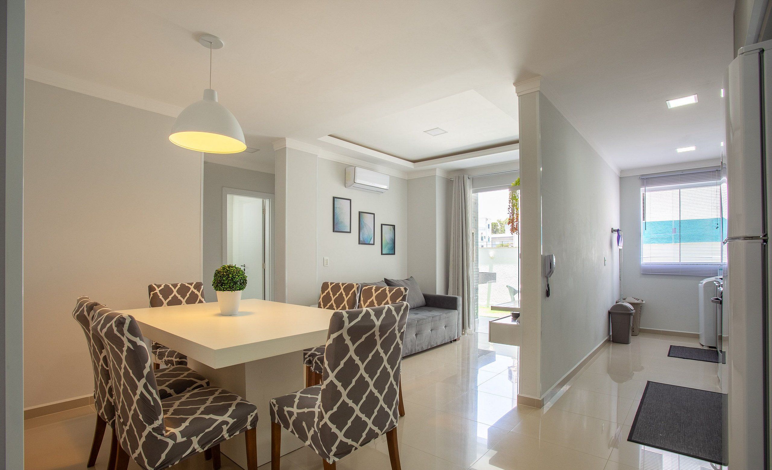 A modern dining area with a white table and patterned chairs, a pendant light, and a view to the outside.