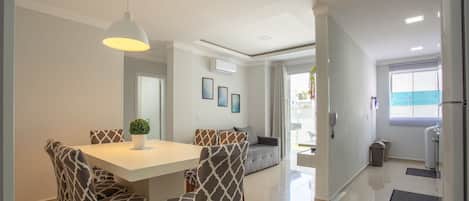 A modern dining area with a white table and patterned chairs, a pendant light, and a view to the outside.
