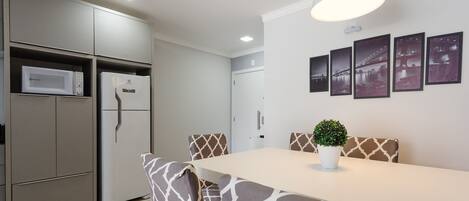 A modern kitchen with built-in appliances, a dining area with patterned chairs, and a wall-mounted light fixture.