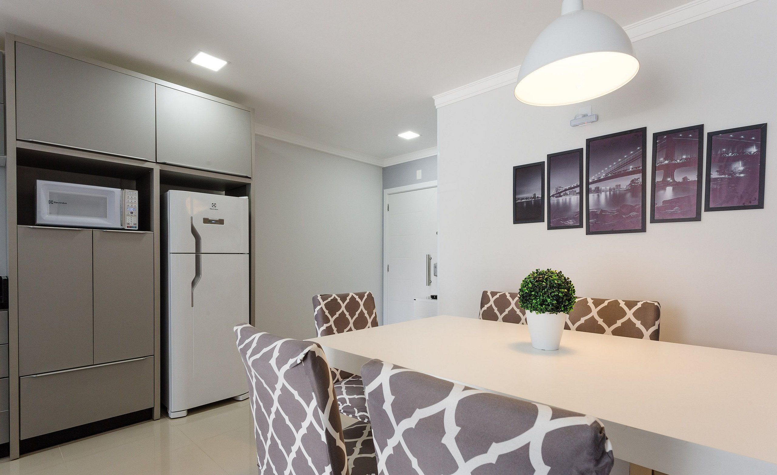 Una cocina moderna con electrodomésticos integrados, una zona de comedor con sillas estampadas y una lámpara fijada a la pared.