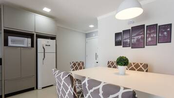 Una cocina moderna con electrodomésticos integrados, una zona de comedor con sillas estampadas y una lámpara fijada a la pared.