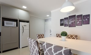 A modern kitchen with built-in appliances, a dining area with patterned chairs, and a wall-mounted light fixture. - Beautiful Seaside Apartment With Barbecue Rmi0007 (Florianópolis)