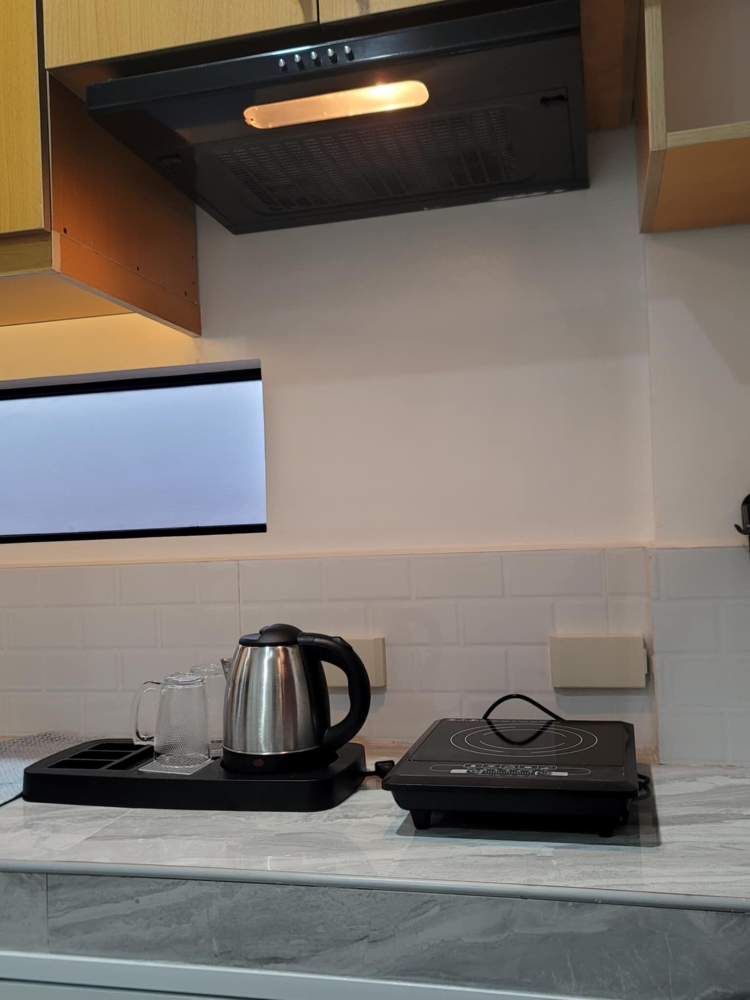 Una cocina con cocina de inducción negra, un hervidor y una cafetera sobre una encimera de mármol.