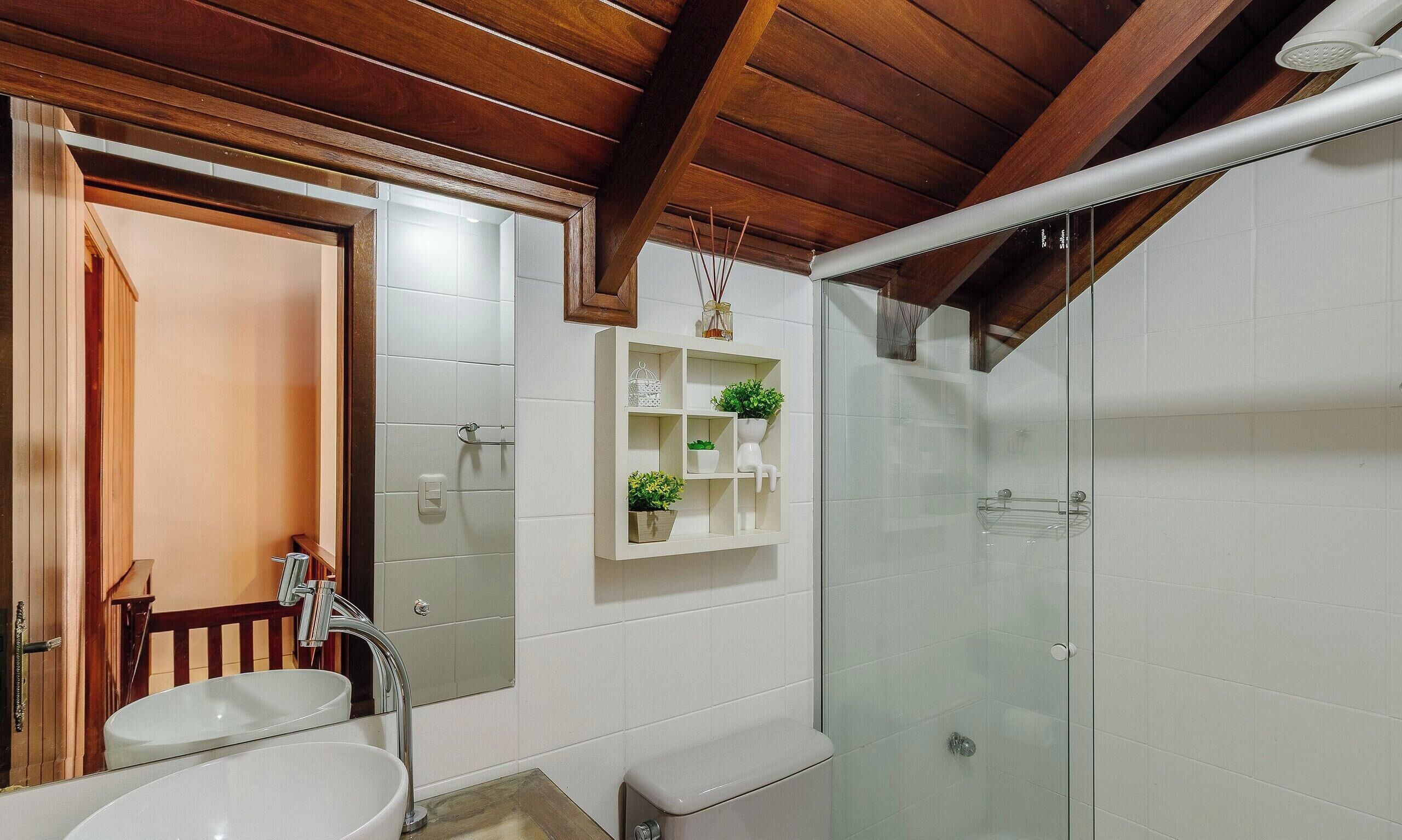 A bathroom with a glass-enclosed shower, a white sink, and a wooden ceiling.